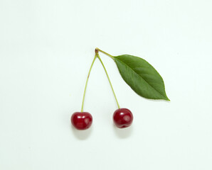 Close-up of two ripe red cherry berries with a cherry leaf isolated on a white background