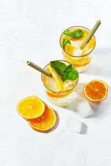 Top view of glassas of summer trendy sparkling cocktail with gin and cold tonic, orange, mint, ice cubes with bamboo straw, garnished with slices orange on white background with copy space.