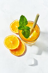 Flat lay of glass of summer trendy sparkling lemonade with orange, mint, ice cubes with bamboo straw, garnished with slices orange on white background.