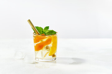 Glass of summer trendy sparkling cocktail with gin and cold tonic, orange, mint, ice cubes with bamboo straw, garnished with slices orange on white background with copy space.