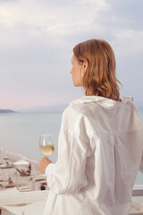 Fototapeta na wymiar Young woman with white wine glass enjpying sunset view in beach bar during summer vacation