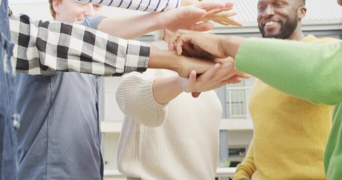 Smiling diverse male and female business colleagues stacking hand and motivating in office