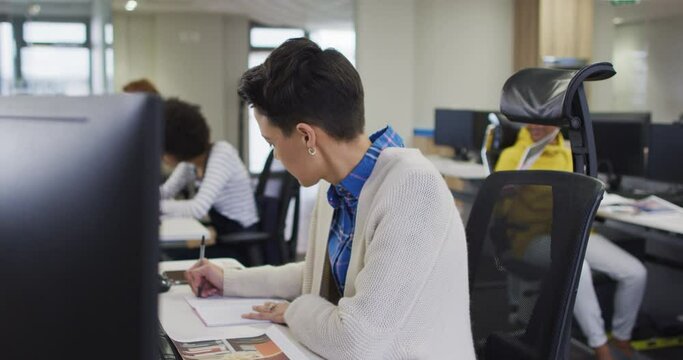 Portrait of caucasian creative businesswoman writing by desk in modern office