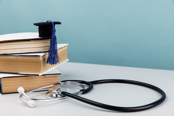Medical education and healthcare theme. Stethoscope and graduation cap on stack of books on blue...