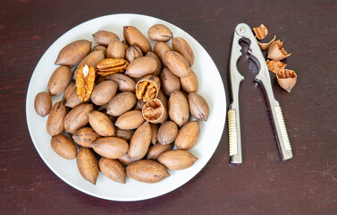Pecan nut, (Carya illinoinensis), top view on white plate on rustic wooden table with nutcracker on the side.