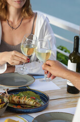 Happy couple toasting with white wine glasses while having dinner during summer vacation