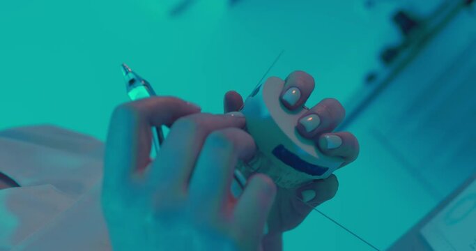 A close-up female orthodontist is applying an archwire to the ceramic model on the teeth and then using dental forceps for clenching and bending the archwire.