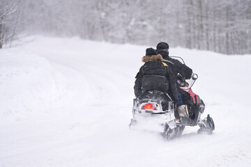 Two men are racing on a snowmobile through snowdrifts in the forest. Snow is falling. Selective focus. Copy space.