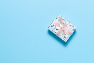Small gift box with pink ribbon bow on blue background