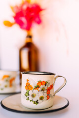 Xícara vintage esmaltada com detalhes de flores e flores ao fundo