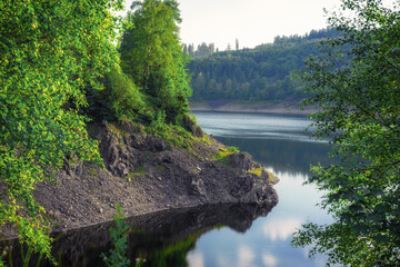 A stony rock wall by the water, behind it are green trees