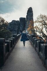 A woman in a coat walks across the Bastei bridge in Saxon Switzerland in the autumn, Germany, back...