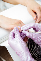 Woman manicurist master is pushing cuticle on client's fingers using wooden stick, hand closeup.