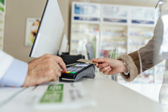 Payment of drug bills. A close-up of the payment terminal at the counter and sweeping the card for the purchase of medicines in the pharmacy. Female and male hands in focus