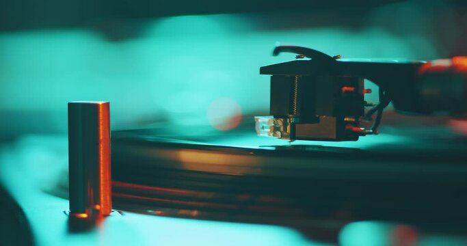 Vinyl record spinning on player. Turntable stylus on record, close-up in colorful neon studio light.