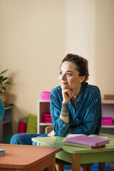 happy teacher looking away near books in montessori school
