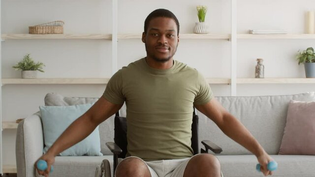 Impaired Black Guy Exercising With Dumbbells In Wheelchair At Home