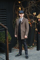 A man posing in the image of an English retro gangster of the 1920s dressed in Peaky blinders style near old brick wall.