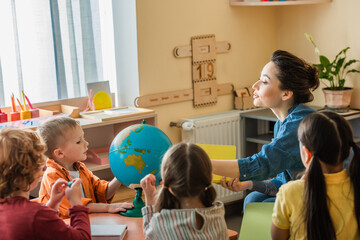 young teacher talking to children near globe during lesson