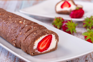 Chocolate roll with curd cream and strawberries inside. Strawberry dessert on the home wooden table. Close up