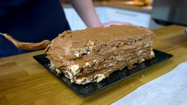 The cook spreads chocolate cream on the bottom level of the meringue cake. The process of making a chocolate tort with nuts and cream. cooking at home.