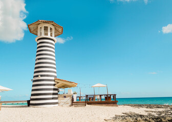 Paisaje de un restaurante con un faro a un lado, a la orilla de la playa