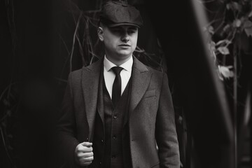 A man posing in the image of an English retro gangster of the 1920s dressed in a coat, suit and...