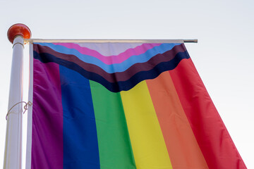 Progress pride flag (new design of rainbow flag) waving in the air with blue sky, Celebration of gay pride, The symbol of lesbian, gay, bisexual and transgender, Worldwide LGBTQ community concept.