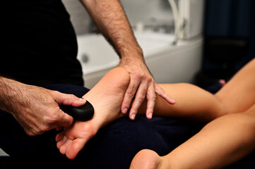 Feet massage with volcanic hot stone in Ayurvedic wellness spa center. Total body restoration concept - obrazy, fototapety, plakaty