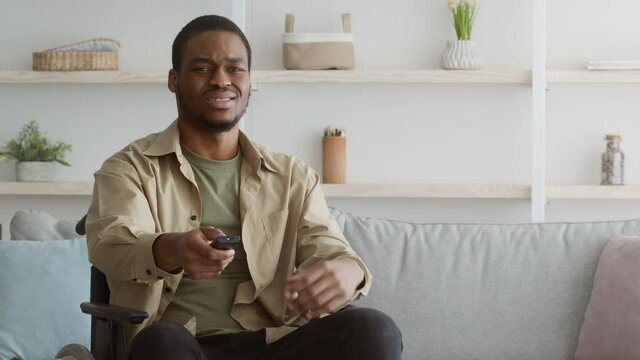 Displeased Disabled Black Guy Watching TV Switching Channels At Home