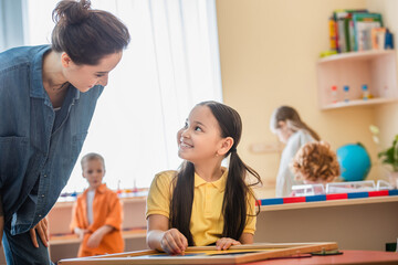 cheerful asian girl combining puzzle near teacher and kids on blurred background
