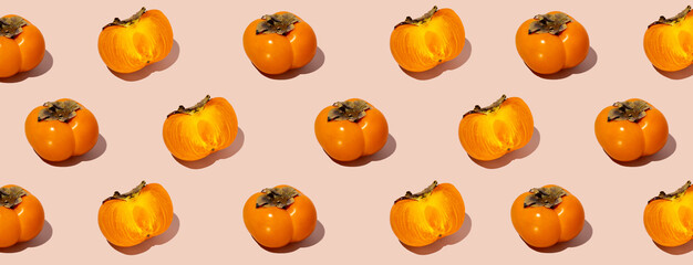 Colorful fruit pattern of fresh whole and sliced organic persimmon fruit with leaves on beige-pink background. Healthy eating and food concept. Flat lay, top view. Design element