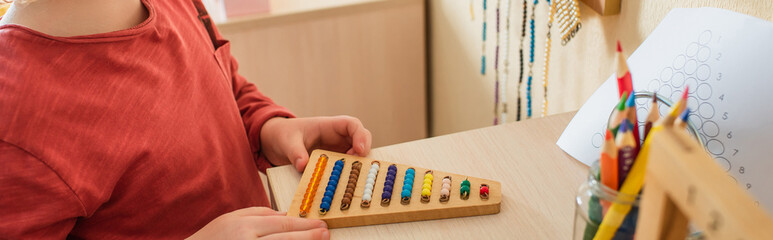 cropped view of boy playing with colorful beads game in montessori school, banner
