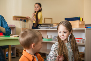 children talking in classroom near teacher and asian girl on blurred background