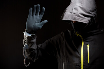 Closeup view of the hands of a burglar or hucker in black gloves with handcuffs on a black...