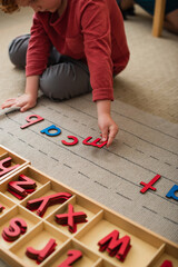 partial view of boy playing with wooden letters on floor in montessori school