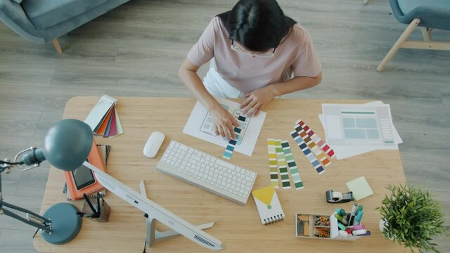 High angle view of young Asian lady designing smartphone application choosing colors working at home alone. Technology and distant work concept.