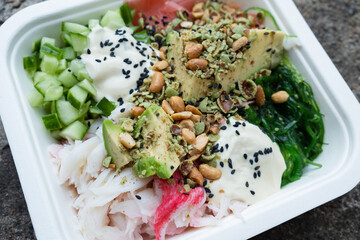 California poke bowl in a white cardboard take away box. Healthy fresh delivery food. Stone background.