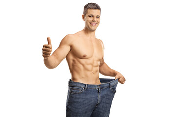 Fototapeta premium Weight loss concept with a young shirtless man wearing oversized jeans and showing thumbs up