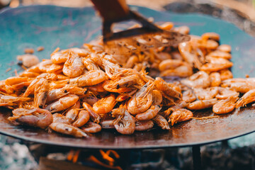 Fried ready-to-eat prawns in a frying pan harrow bbq camping on a background of coals
