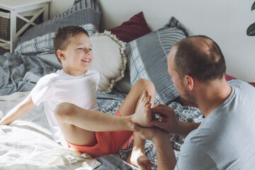 Father plays with his son 7-10 on bed. Dad tickles kids feet. Family, having fun