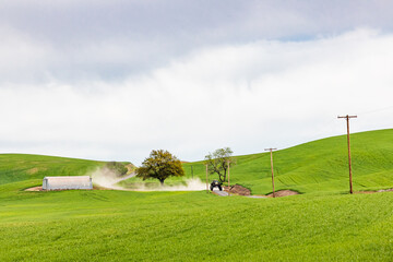 Tractor driving on dirt road through wheat fields in the Palouse hills.