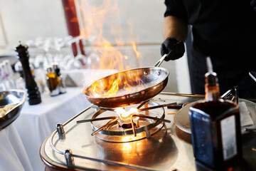 the chef prepares orange caramel on an open fire on the terrace of the restaurant