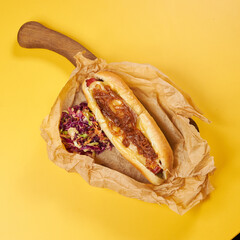 hot dog with pickled onions on a yellow background in craft paper and cabbage salad