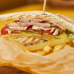sandwich with ham chicken and tomatoes on craft paper and yellow background and fries