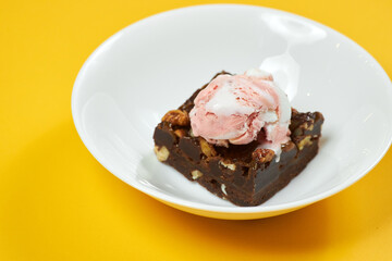 chocolate brownie with ice cream on white plate and yellow background