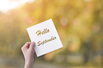 Hand holding paper with Hello September text over blur nature background. Autumn concept.