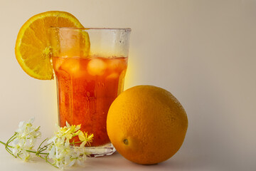 large glass with orange juice and ice a whole orange on a beige background