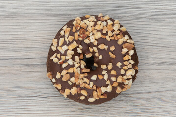 Overhead view of chocolate raised donut is textured with crushed nut coating for a sweet treat delight