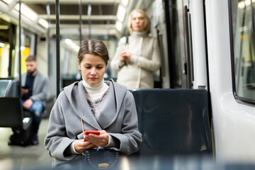 Naklejka na ściany i meble Positive woman reading from mobile phone screen in tram. High quality photo